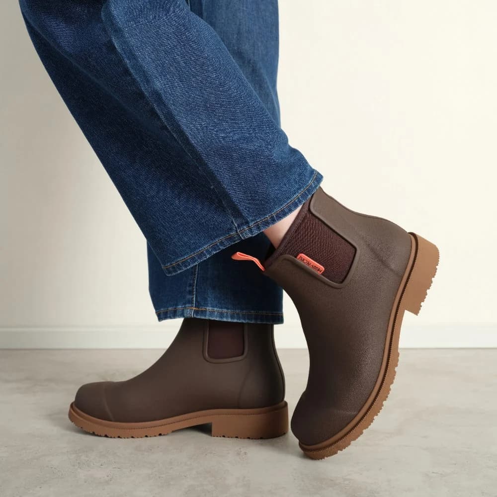 Brown rubber boots worn with blue jeans on a neutral background