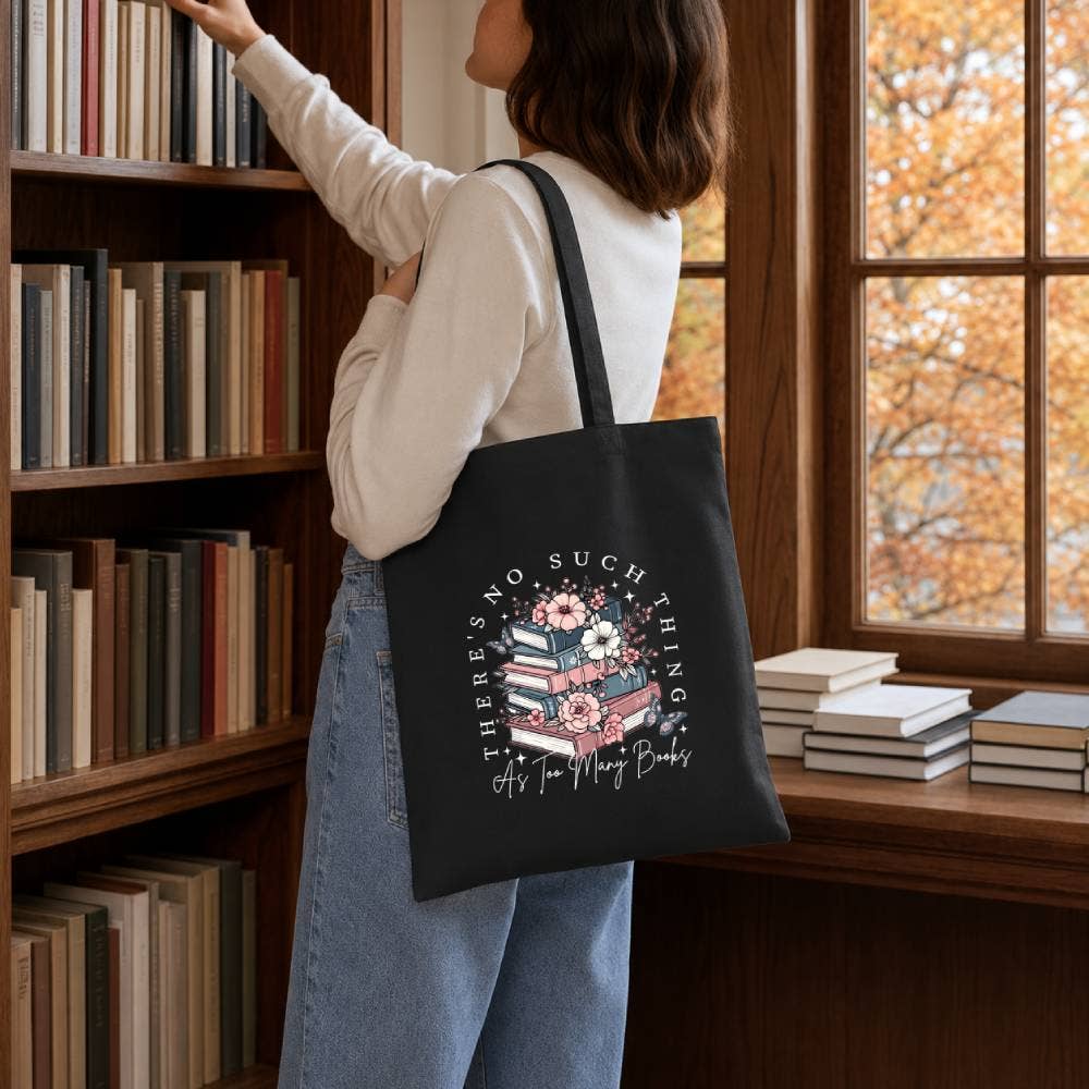 Person holding a black tote bag with a book-themed design in a library setting