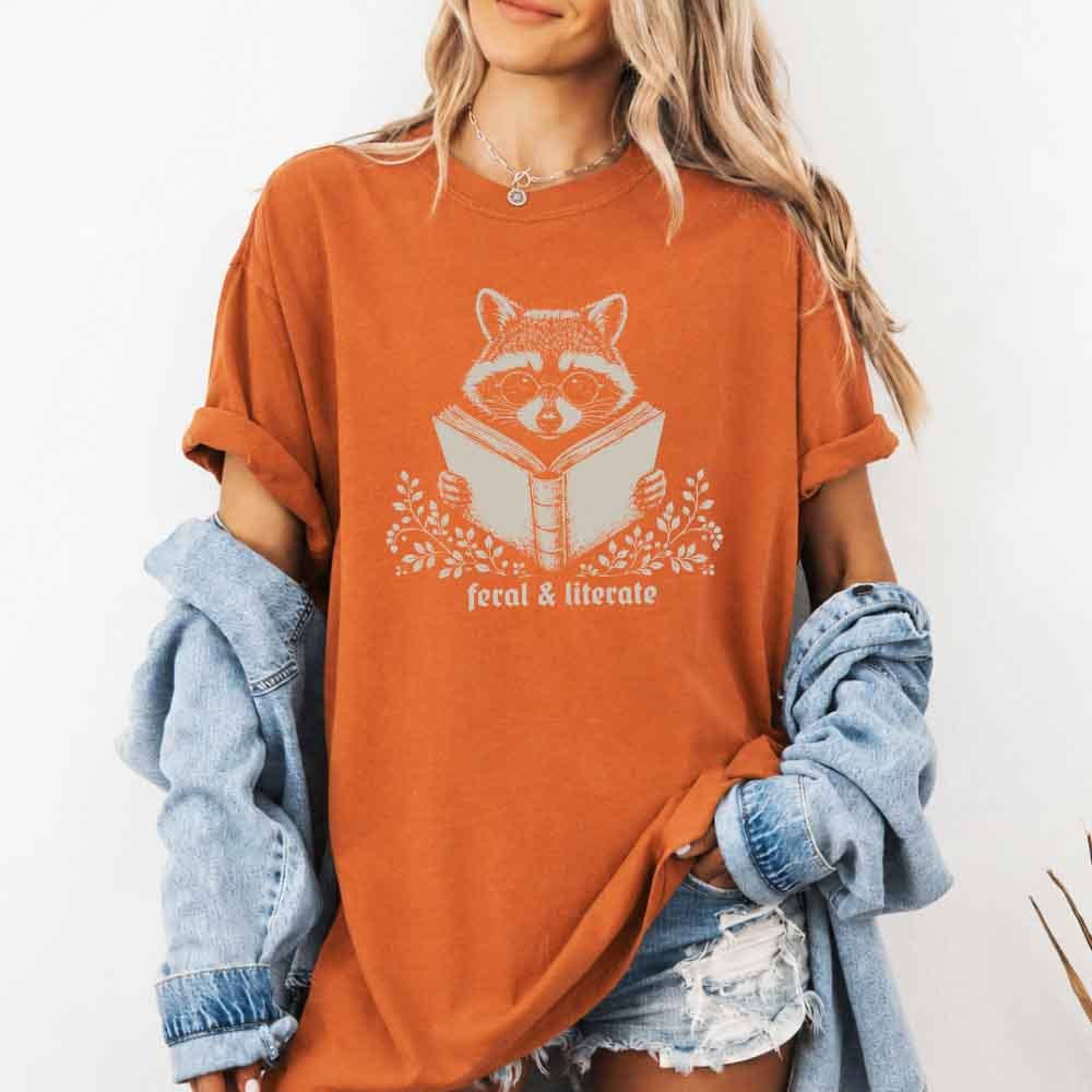 Person wearing an orange t-shirt with a raccoon graphic and text, holding a denim jacket.