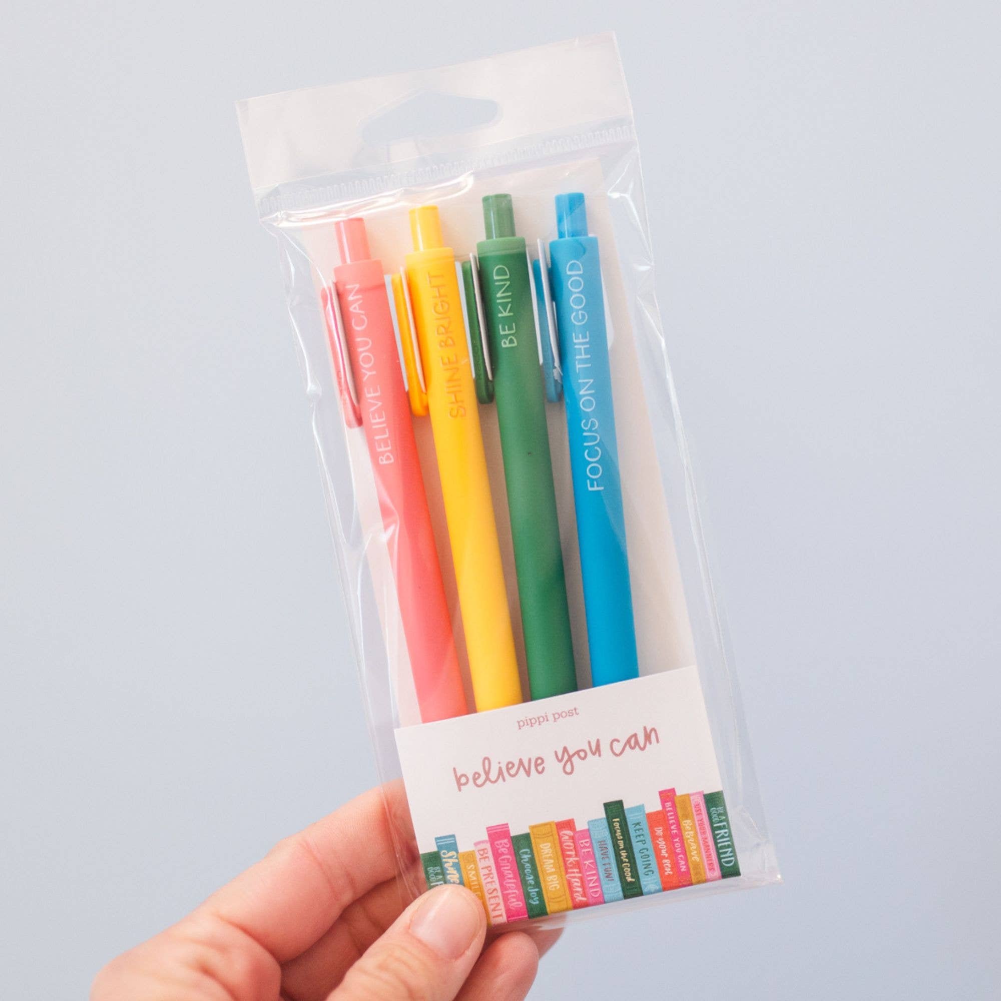 Set of colorful pens in a clear plastic package held by a hand against a light gray background