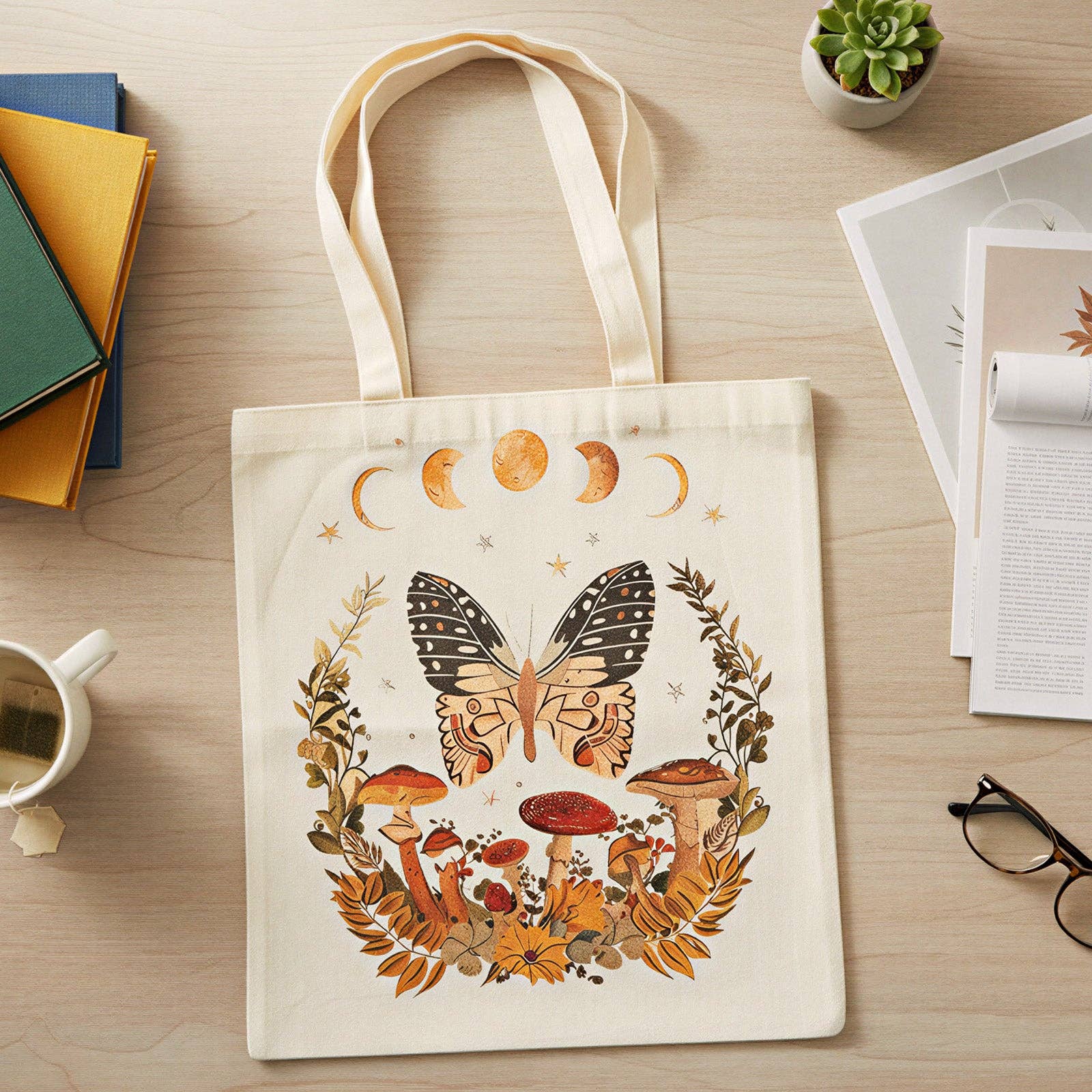 Tote bag with butterfly and mushroom design on a wooden surface with books and a plant.