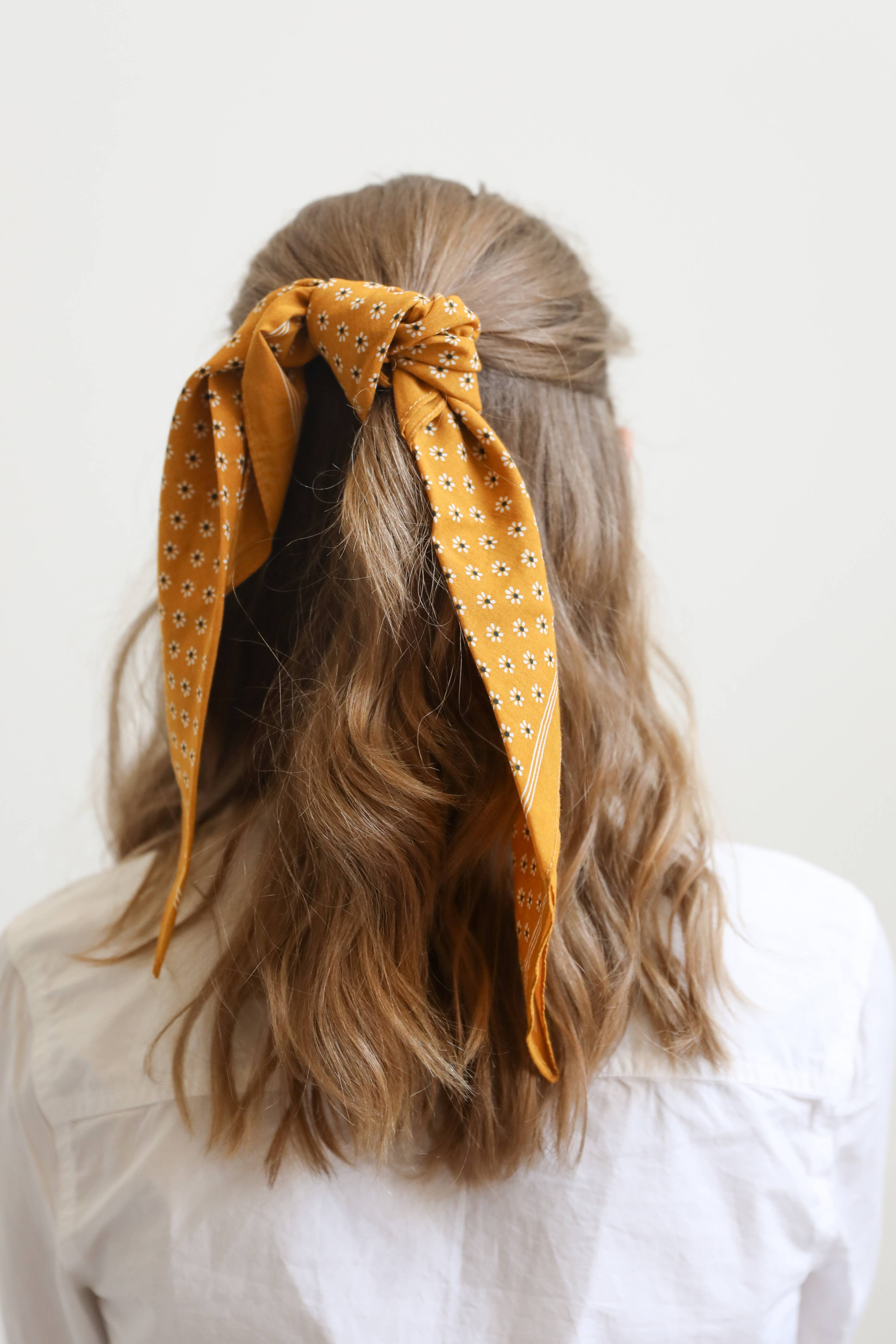 Woman with long hair wearing a yellow patterned headscarf on a white background