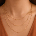 Gold necklace with multiple strands on a person wearing a brown top.