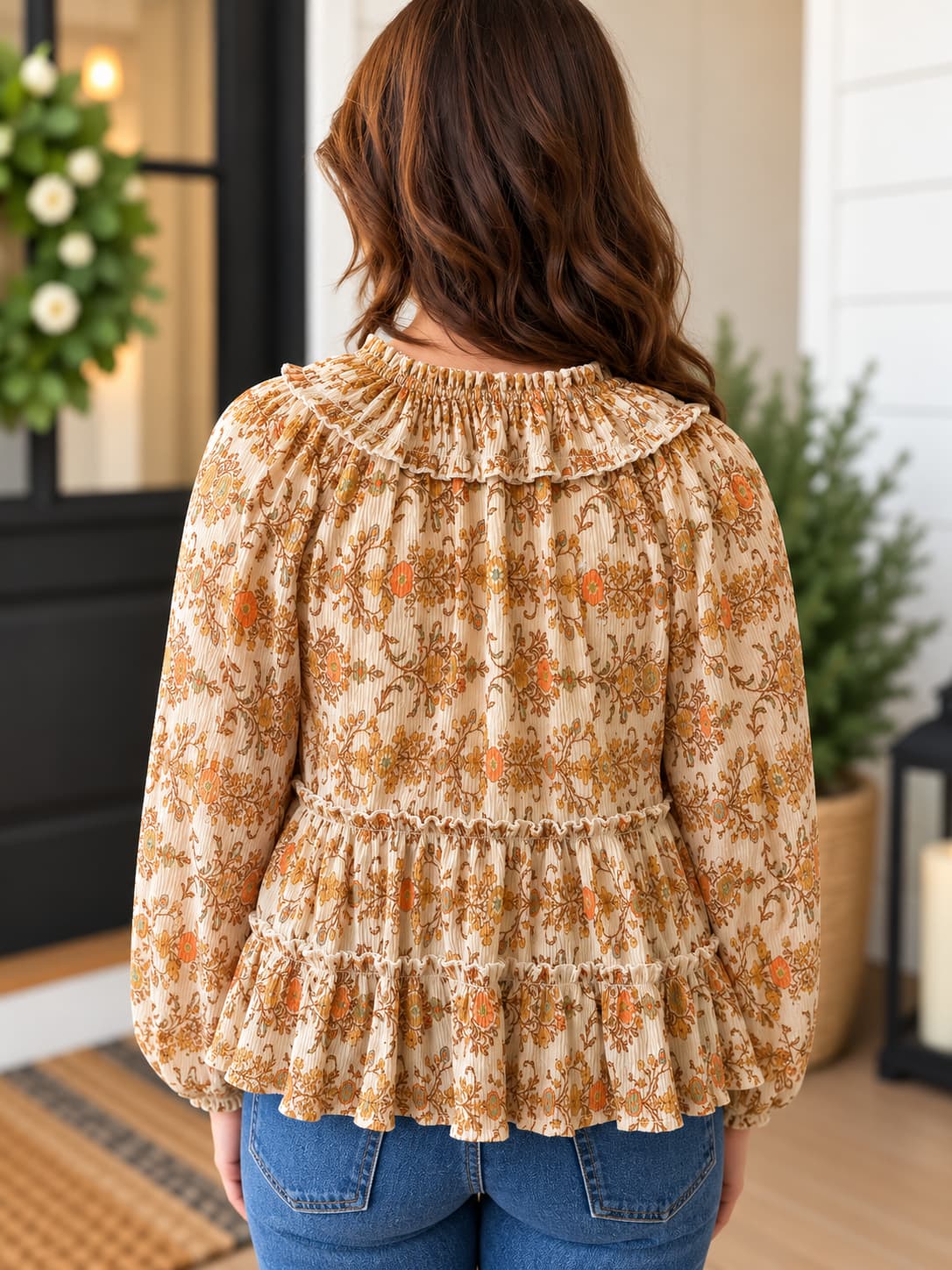 Back view of woman wearing printed boho style peasant blouse top in beautiful orange and tan colors with blue denim.