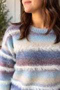 A close-up of a woman wearing a fuzzy knit sweater with horizontal stripes in light blue, cream, mauve, and lavender.