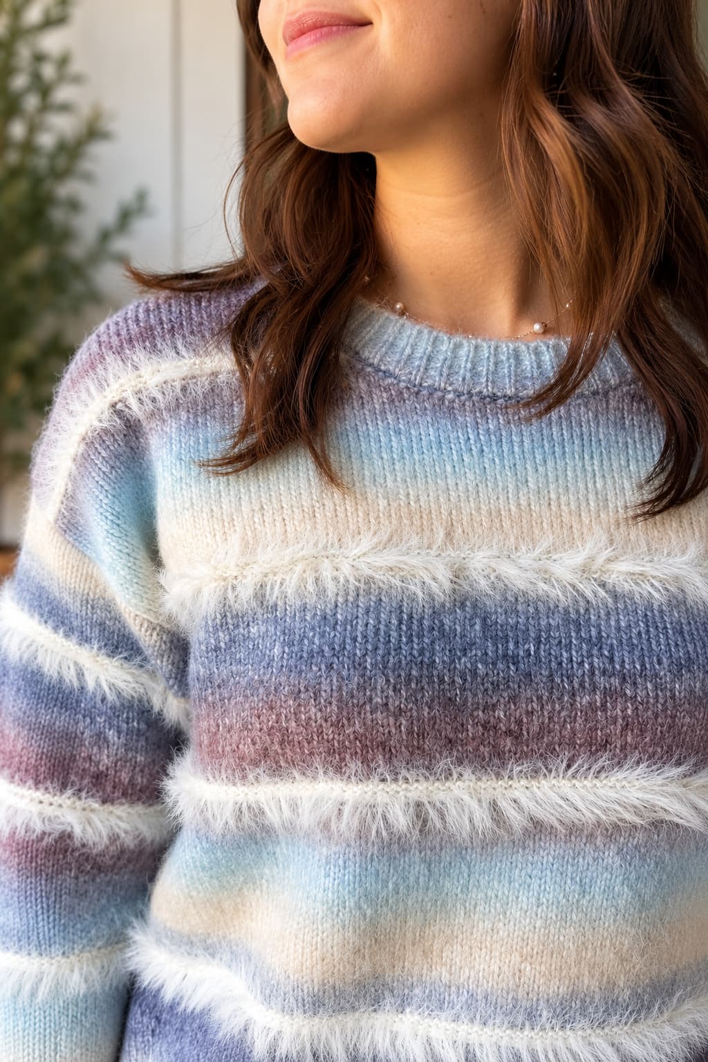 A close-up of a woman wearing a fuzzy knit sweater with horizontal stripes in light blue, cream, mauve, and lavender.