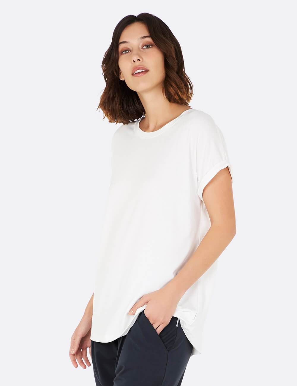 A woman wearing a white short-sleeve crewneck t-shirt and dark pants, photographed against a clean white studio background.