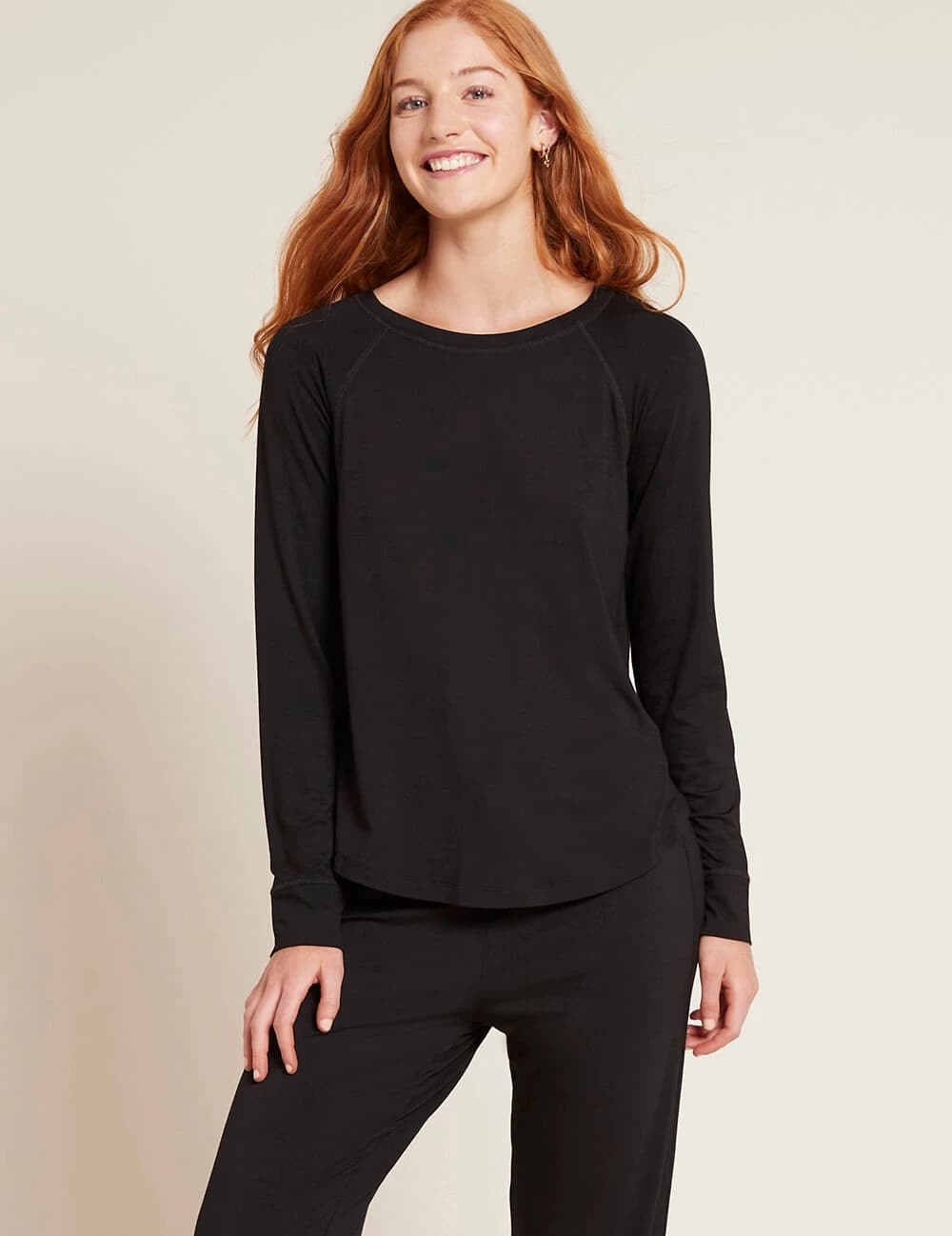 Woman wearing a black long-sleeve top and black pants against a beige background