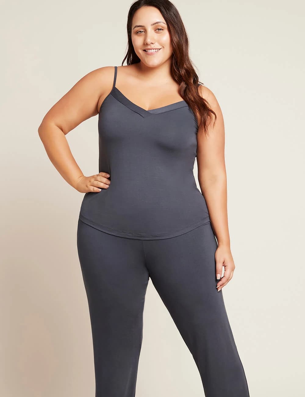 A woman modeling a dark gray ribbed camisole tank top and matching high-waisted leggings against a solid light beige background.
