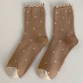 A pair of ankle-high knit socks in a warm taupe brown color, decorated with small white polka dots and featuring a ruffled trim at the top and light beige toes.
