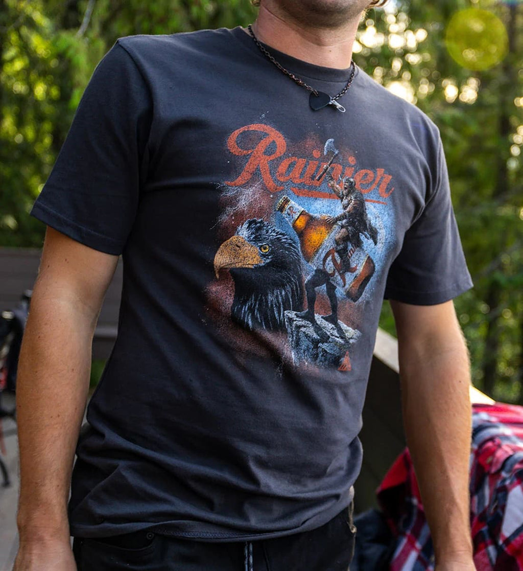 Person wearing a black t-shirt with a graphic design of an eagle and bear, and the word 'Rainier' on it.