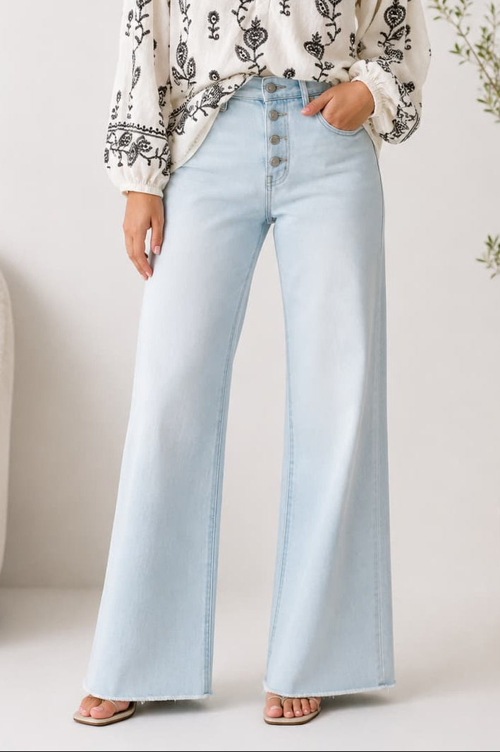 Woman wearing a white blouse with black embroidery and light blue jeans with a button fly in a minimalistic room