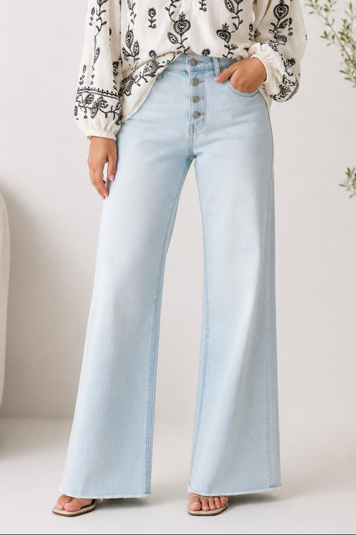 Woman wearing a white blouse with black embroidery and light blue jeans with a button fly in a minimalistic room
