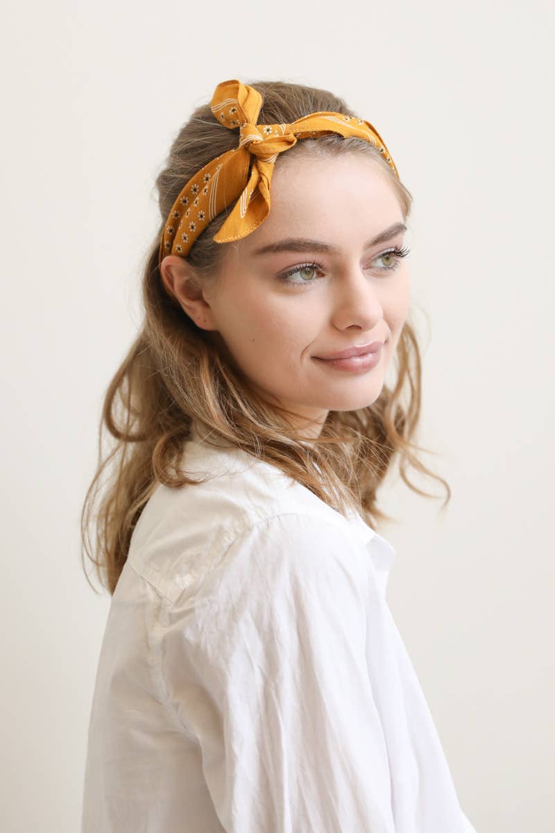 Woman wearing a yellow headband with a pattern against a plain background