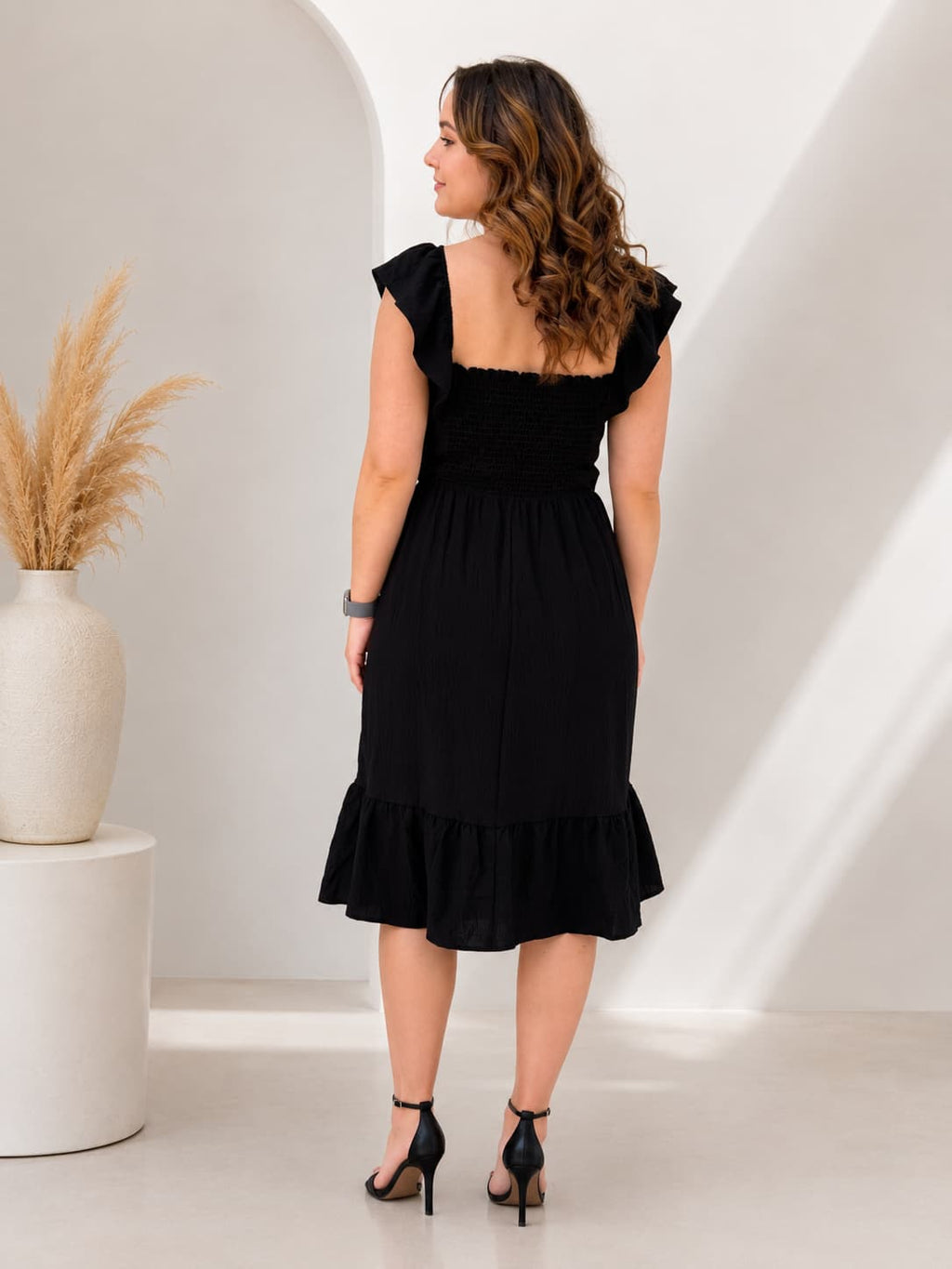 Woman wearing a black dress with ruffled hem in a minimalistic setting