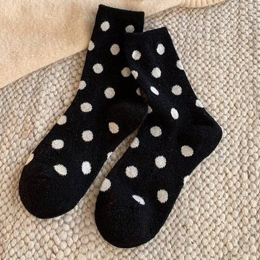 Black socks with white polka dots on a textured surface with a sweater and toy in the background.