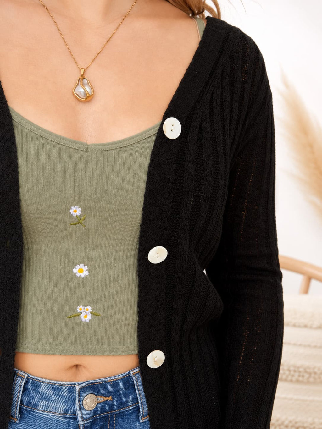 Person wearing a green ribbed tank top with floral designs, black cardigan, and blue jeans.