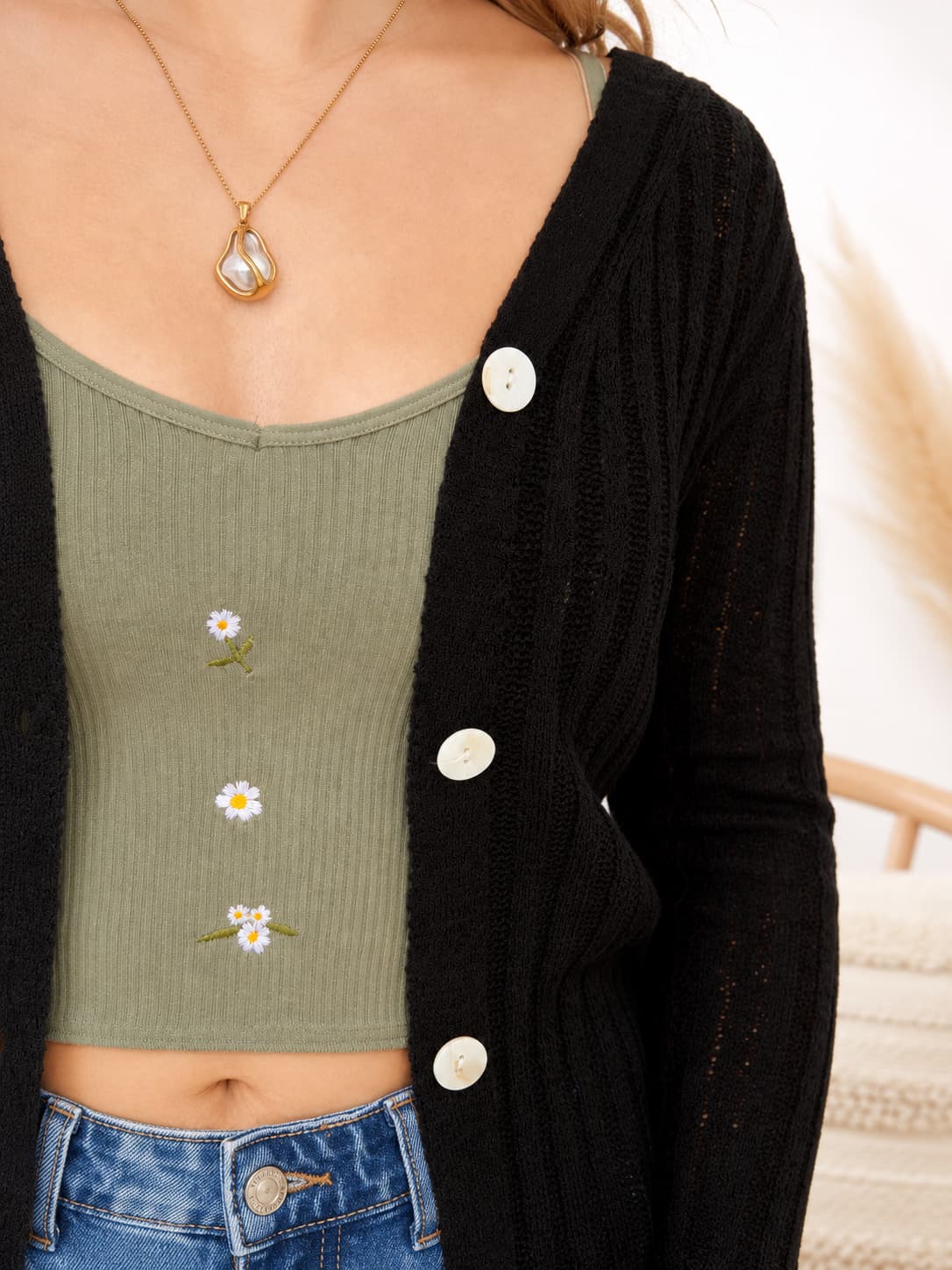 Person wearing a green ribbed tank top with floral designs, black cardigan, and blue jeans.