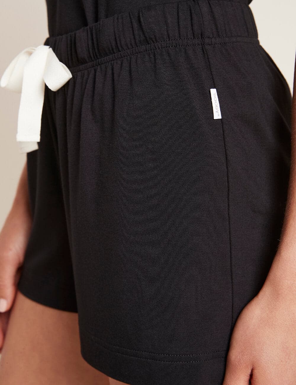 Close-up of a person wearing black textured shorts with a white drawstring on the side and a small white brand tag.