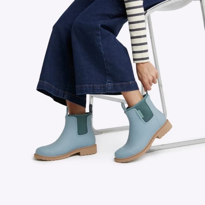 Person wearing light blue rain boots with brown soles on a white background