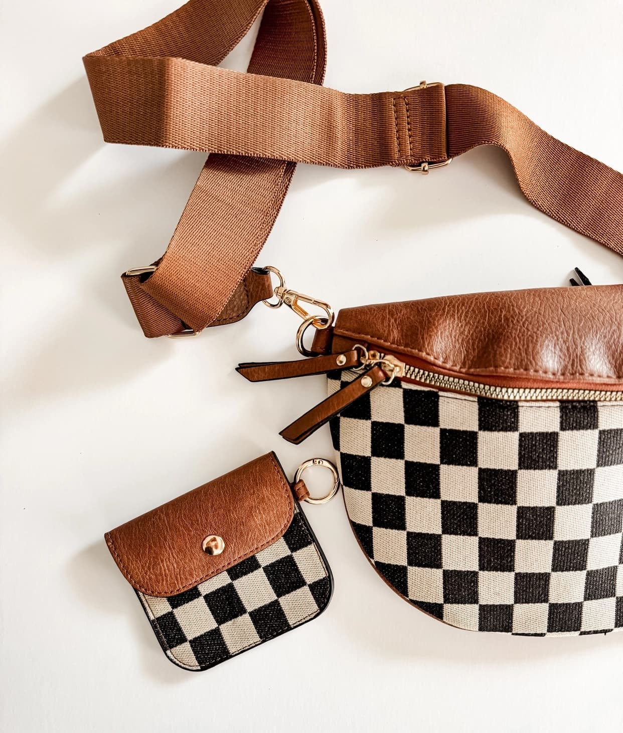 A brown and black checkerboard crossbody bag with a matching small pouch, laid flat on a white background. The bag features a brown leather-look top, a wide brown webbing strap, and a black-and-white checkered body with gold-tone hardware.