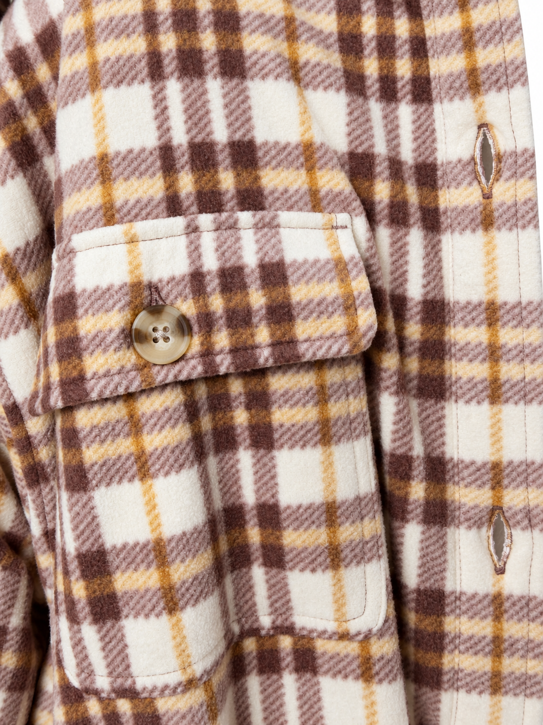 Close-up of a plaid  fleece overshirt fabric with a chest pocket and button, showing a cream base with brown and mustard yellow checks.
