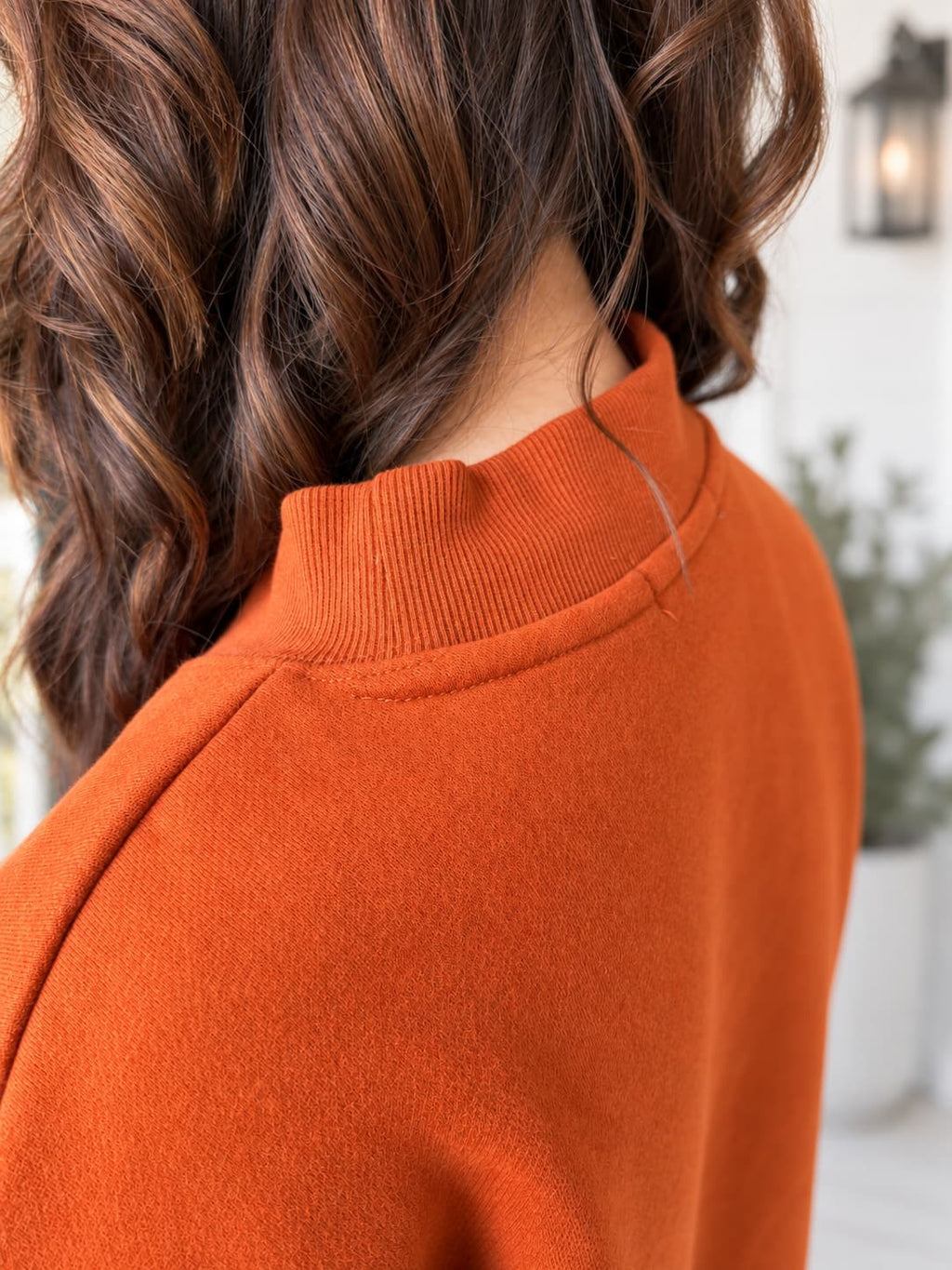 Close-up of a person wearing a ribbed mock neck sweater in a warm burnt orange color, with brown hair visible.