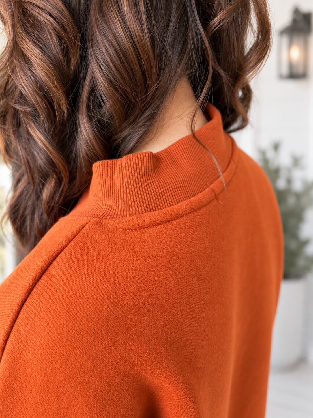 Close-up of a person wearing a ribbed mock neck sweater in a warm burnt orange color, with brown hair visible.