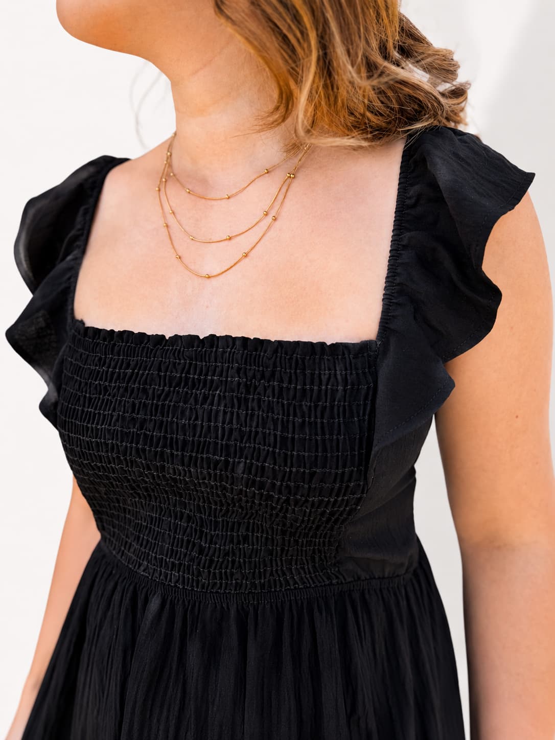 Black dress with ruffled shoulders worn by a person, on a plain background