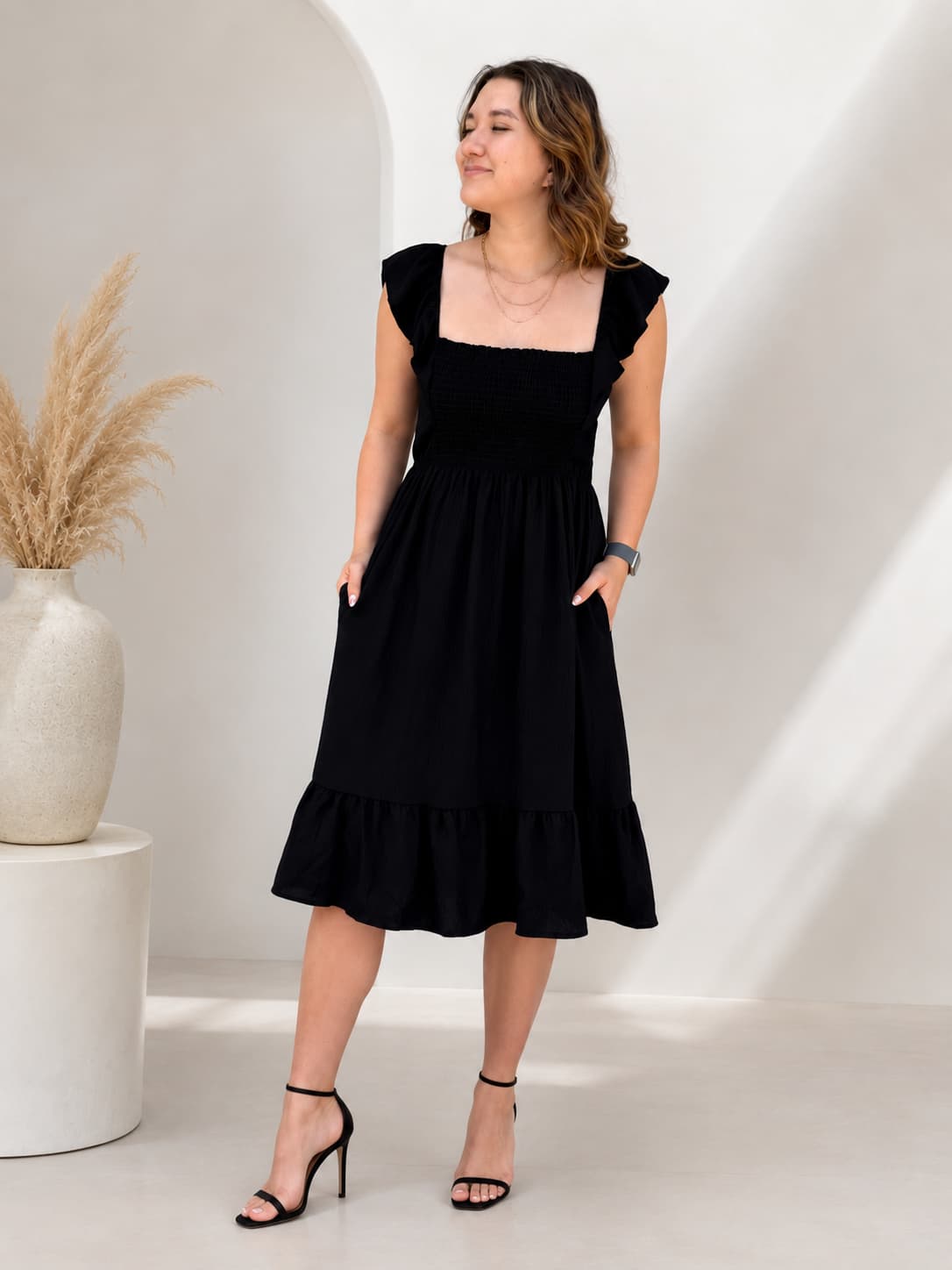 Woman wearing a black dress standing in a minimalistic setting with a vase and decorative elements.