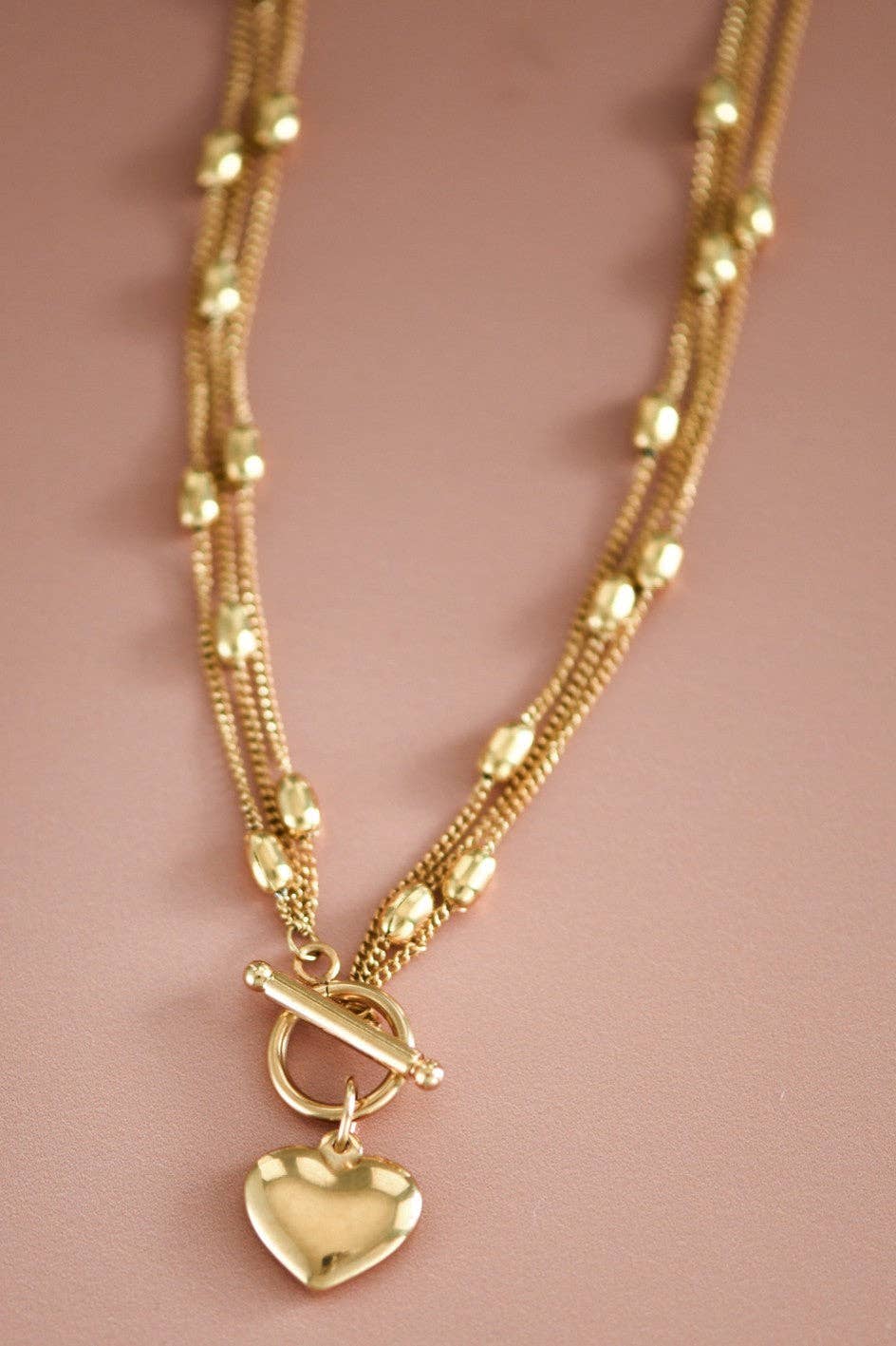 Gold necklace with a heart-shaped pendant on a pink background