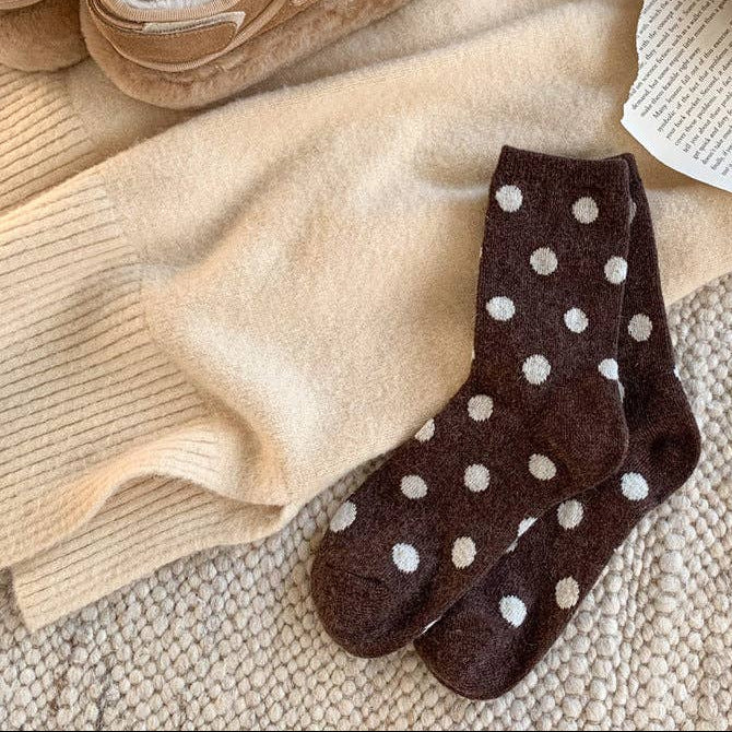 Brown socks with white polka dots on a beige surface with shoes and a book in the background.