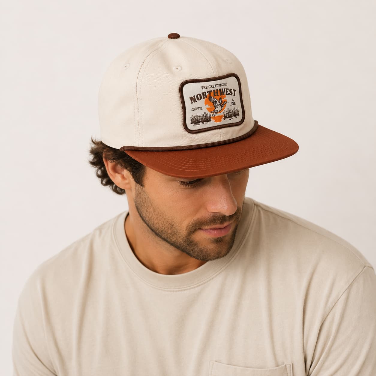 A man wearing a cream-colored snapback cap with a brown brim and a 'Northwest' patch on the front, paired with a matching cream t-shirt against a light off-white background.