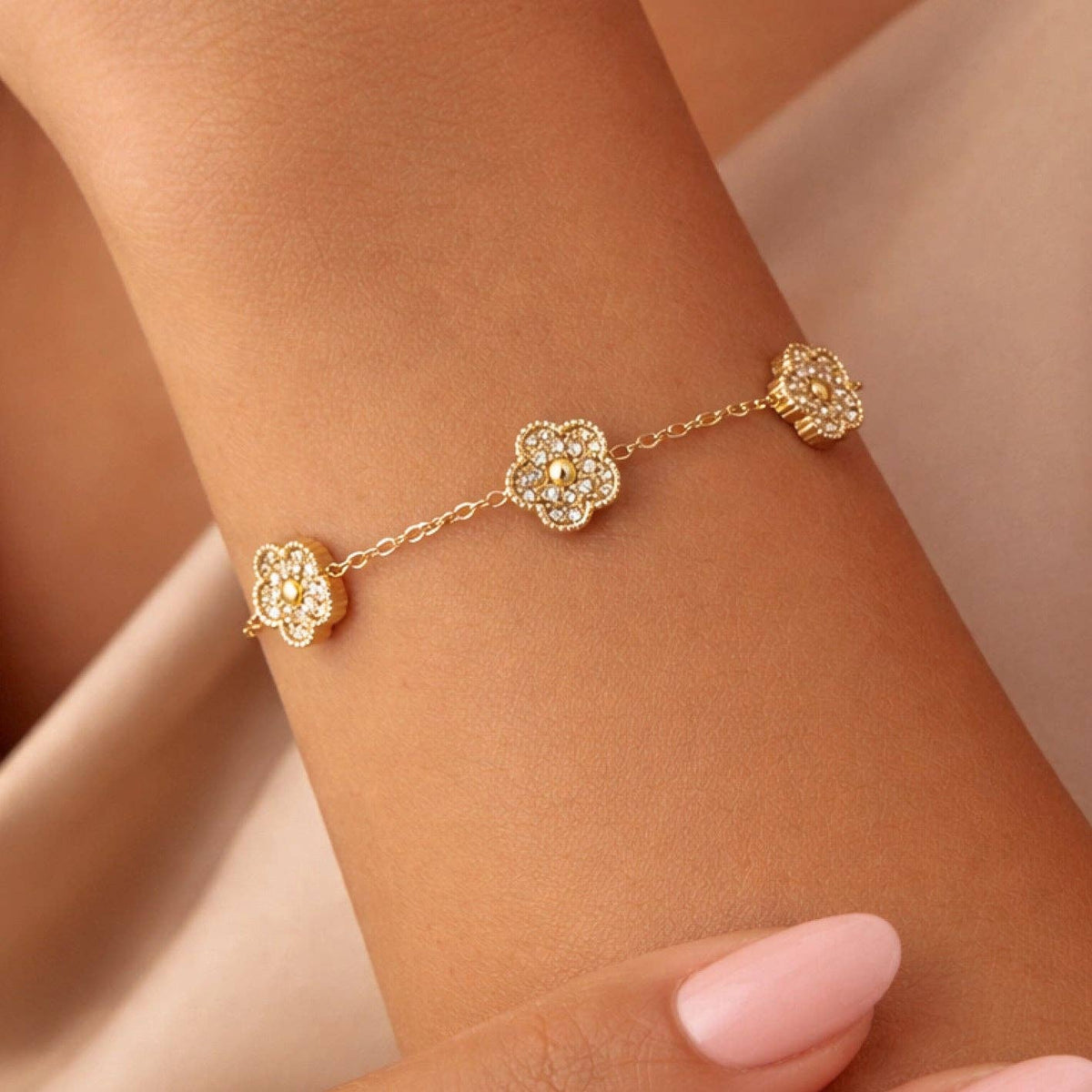 Gold bracelet with floral designs on a wrist against a neutral background