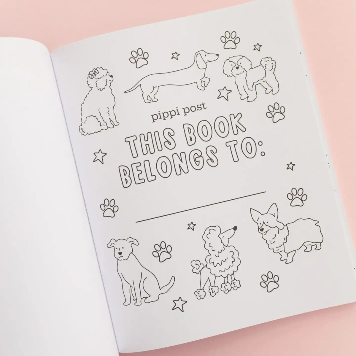 A white coloring book book shown open on a soft pink background, with a printed black-and-white dog-themed page that reads 'pippi post THIS BOOK BELONGS TO:' and includes line drawings of several dogs and paw prints.
