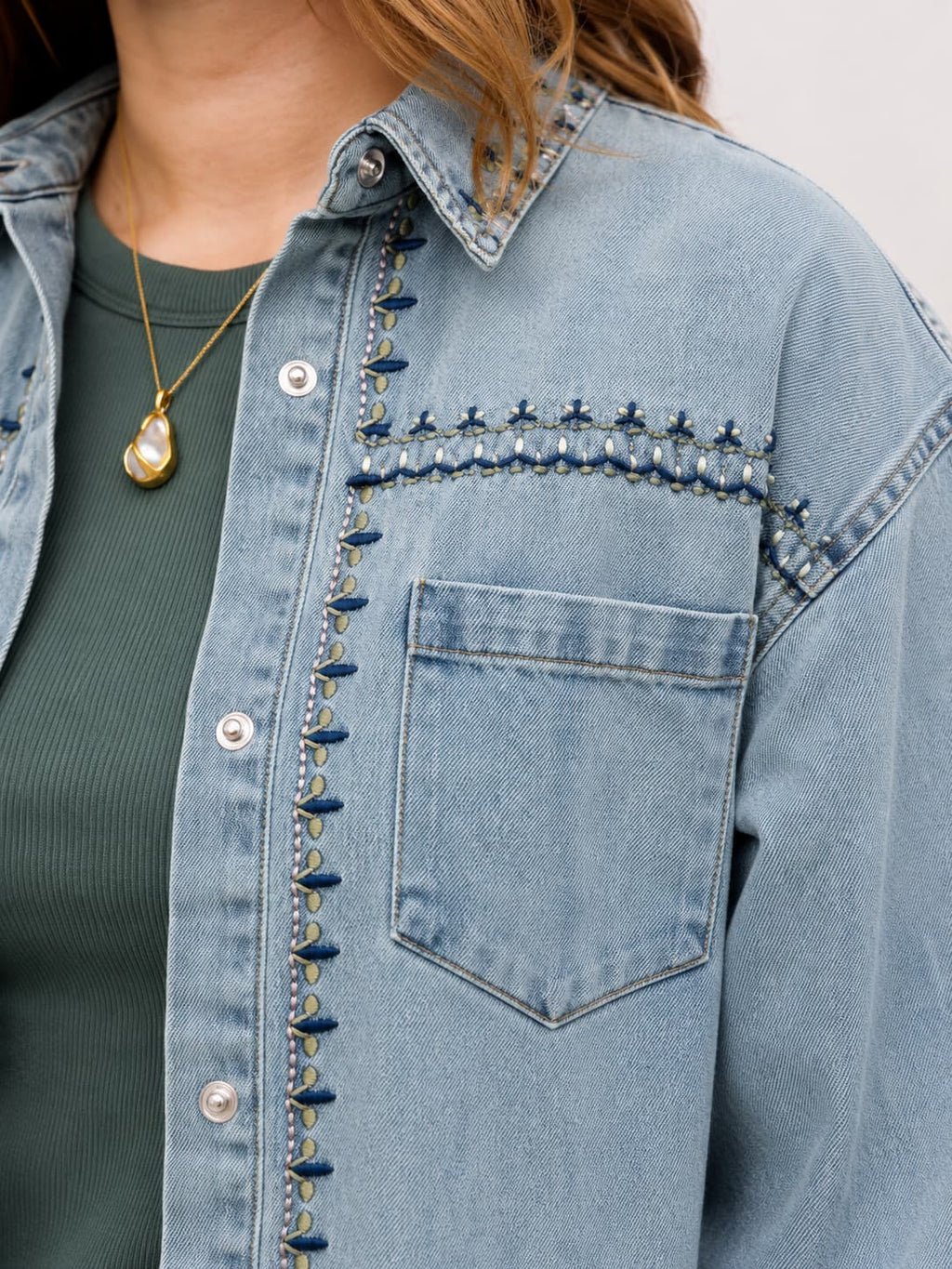 Close-up of a blue denim jacket with decorative embroidery elements and a person wearing it.