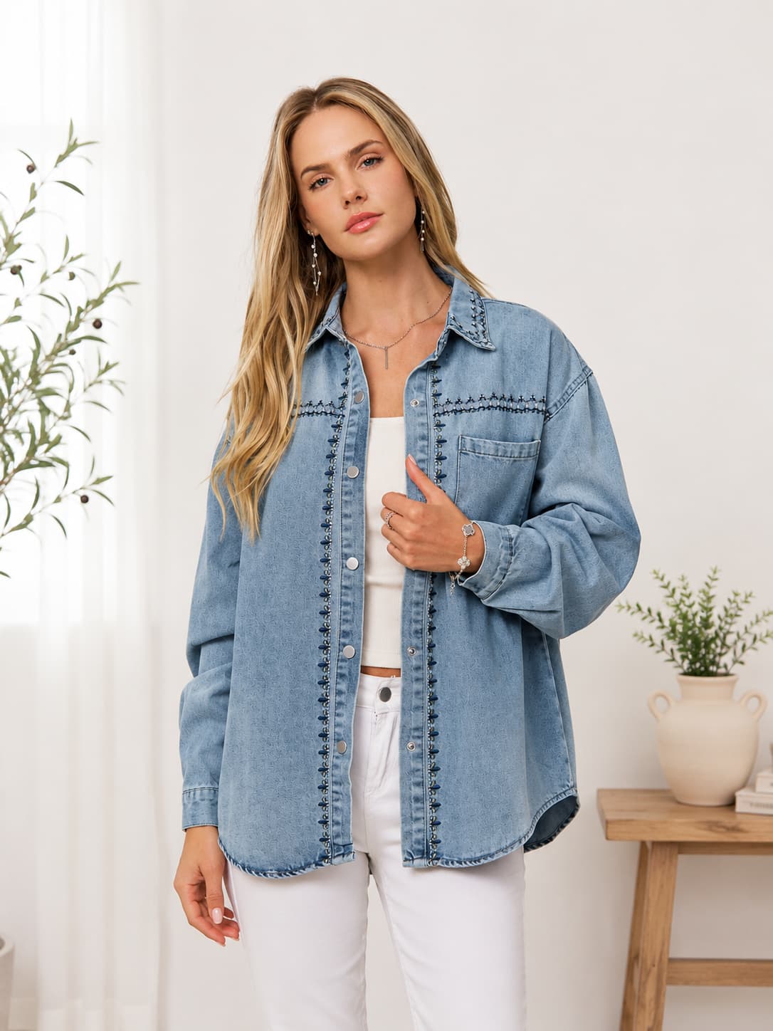 Woman wearing embroidered shirt jacket with white tank and white pants.