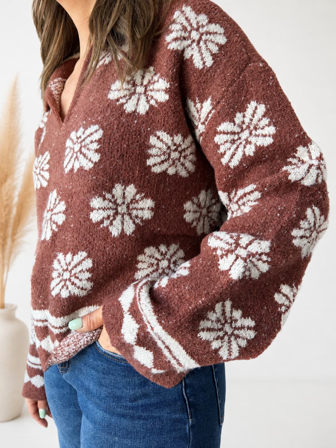 A woman wearing a brown fuzzy knit sweater with a white snowflake pattern, paired with blue jeans, shown in a close-up lifestyle shot.