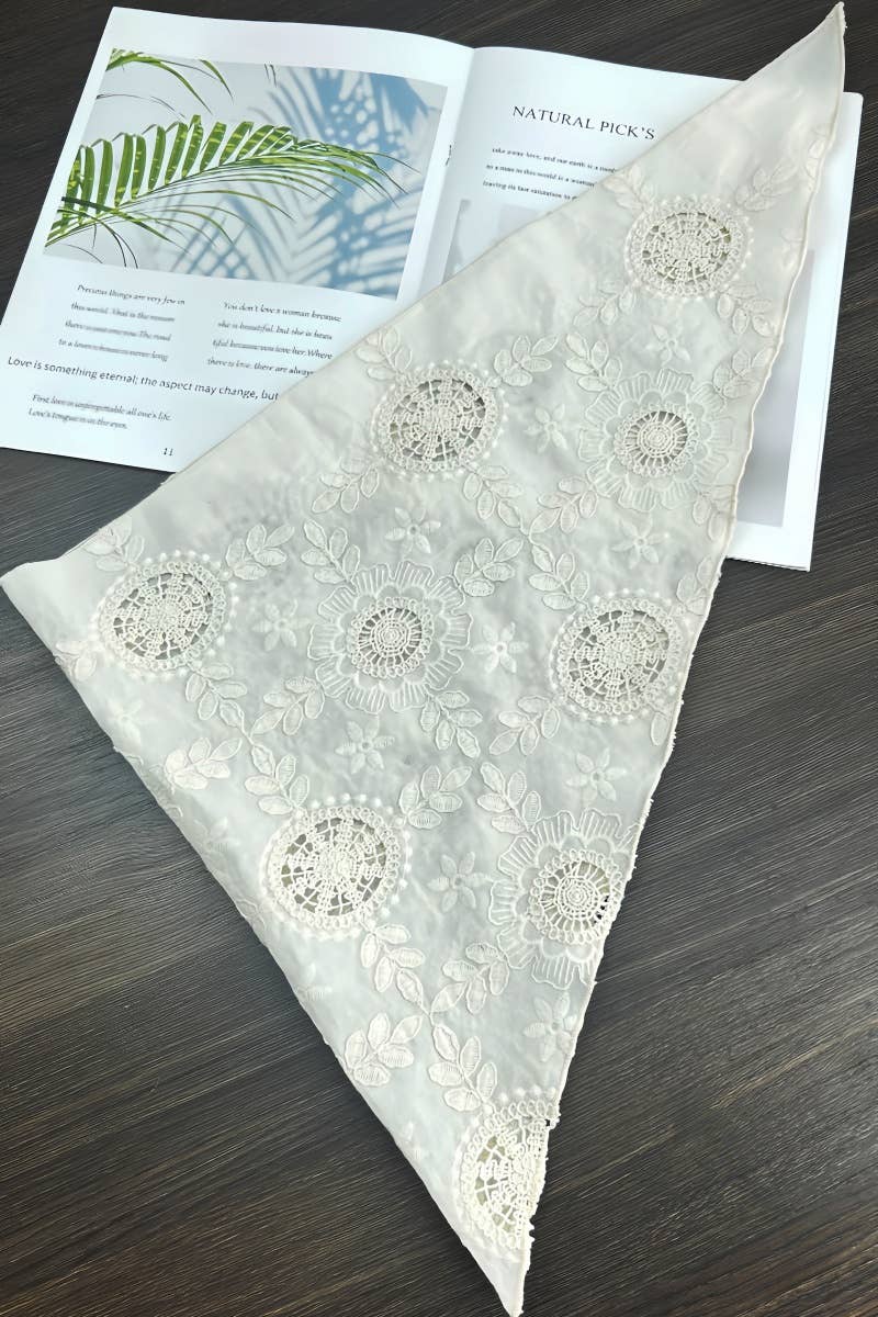 White lace fabric with floral patterns on a wooden surface with a magazine underneath.