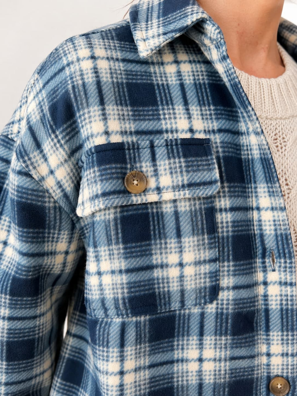 Close-up of a person wearing a blue and white plaid button-up shirt with a chest pocket and a cream knit sweater underneath.
