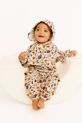 A baby wearing a matching hooded sweatshirt and pants set with a floral and football print, sitting on a white curved studio prop against a white background.