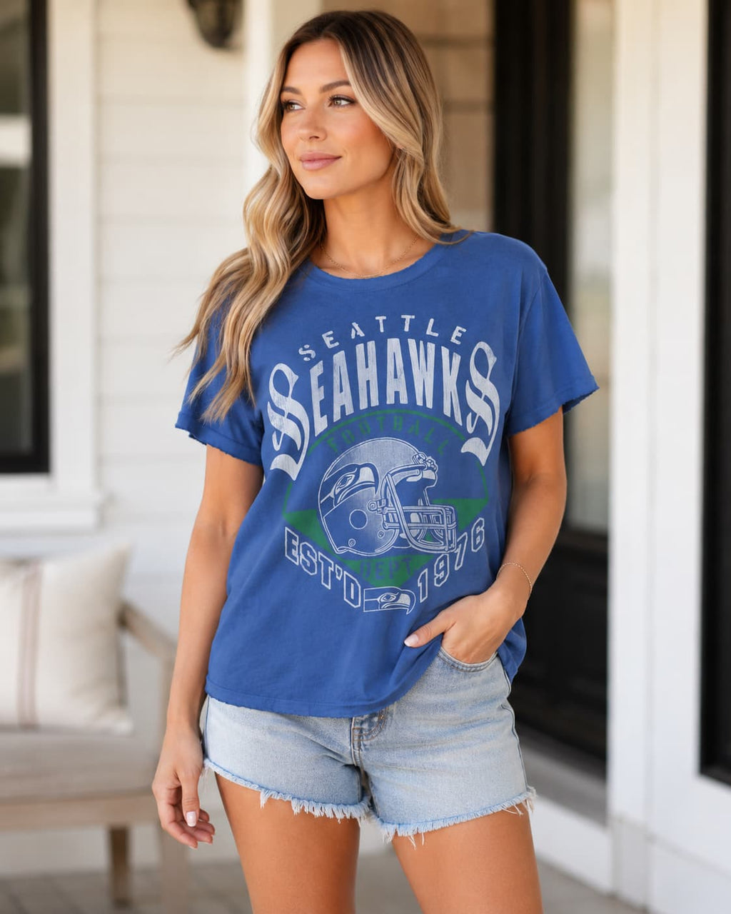 A woman modeling a blue Seattle Seahawks graphic t-shirt with light-wash denim shorts, standing on a porch.