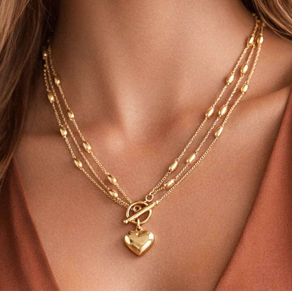 Gold necklace with heart pendant on a person wearing a rust-colored top.