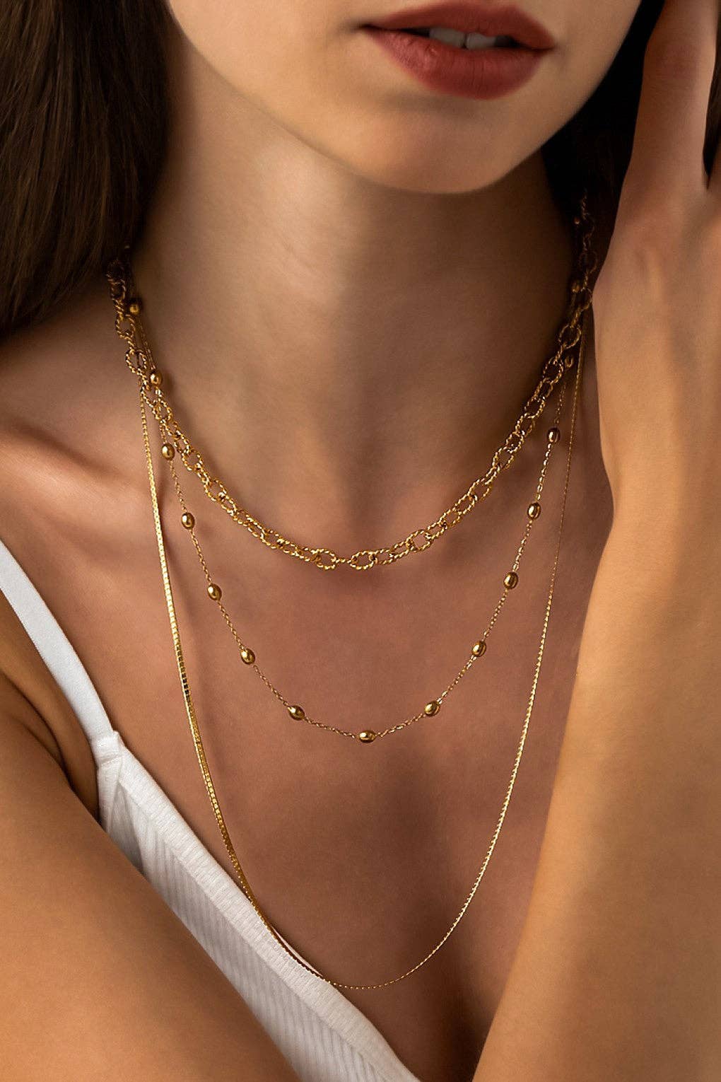 Close-up of a woman wearing gold necklaces with a neutral background
