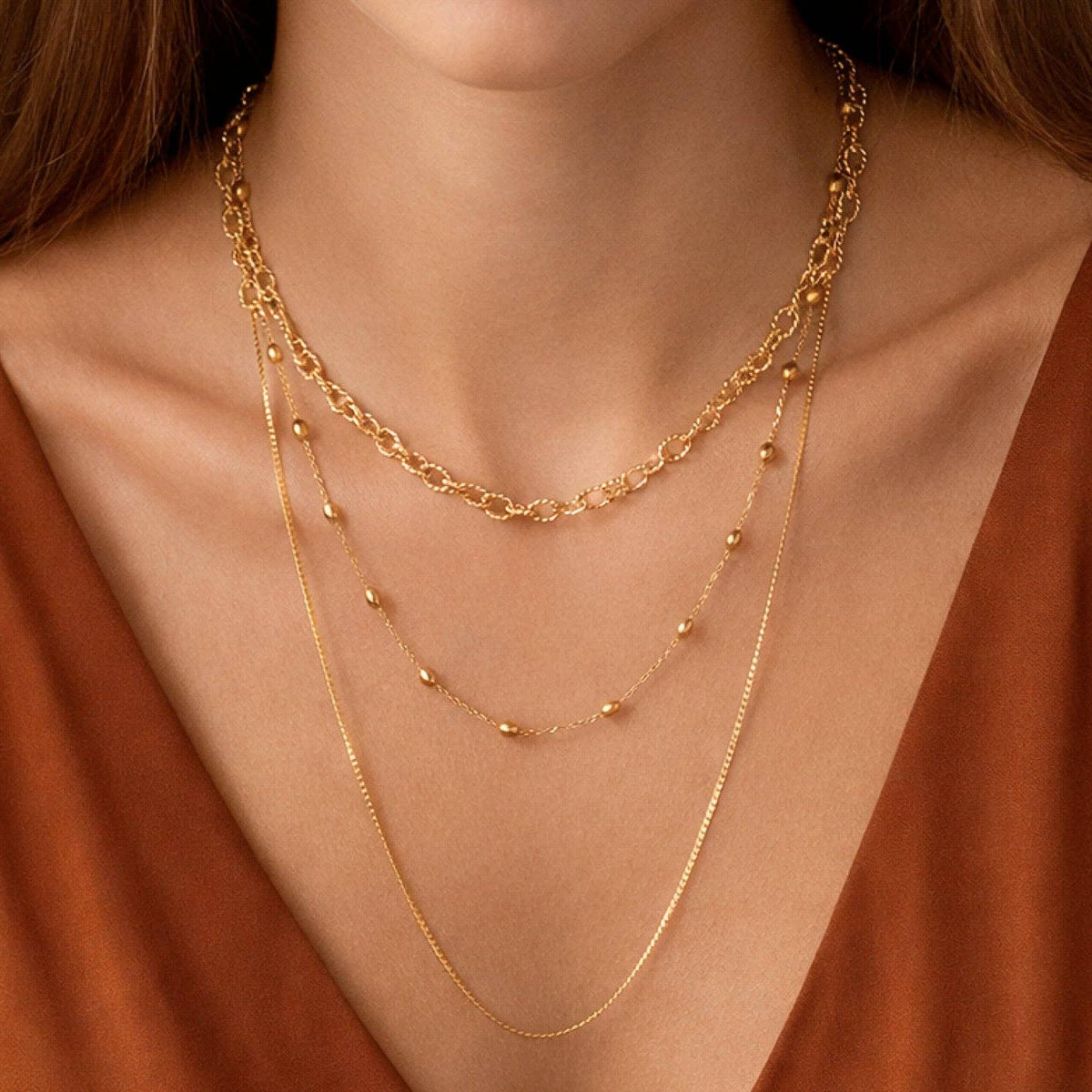 Close-up of a person wearing a gold necklace with a brown background