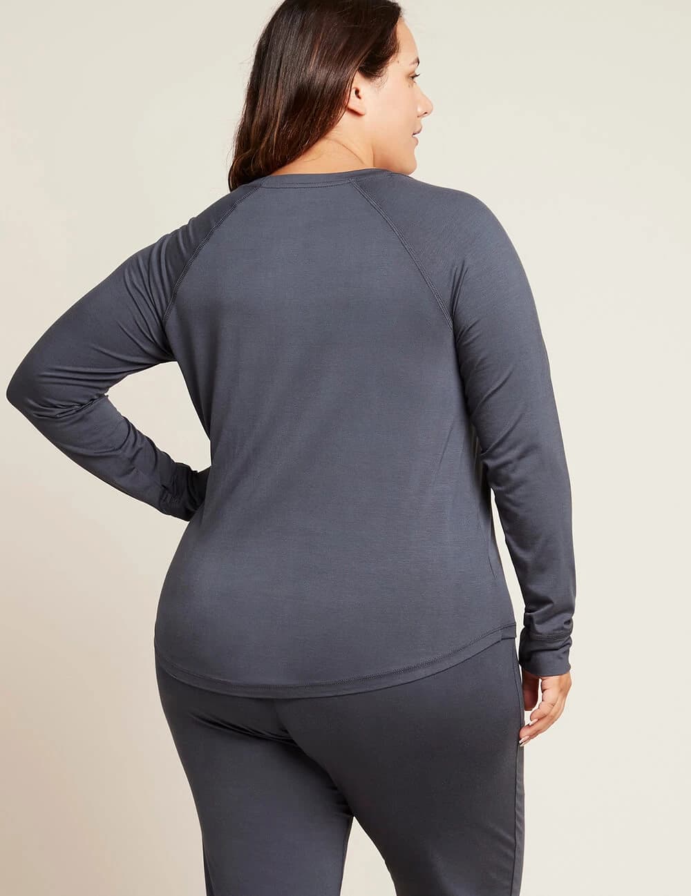 A woman shown from the back wearing a dark gray long-sleeve athletic top and matching leggings against a plain light beige studio background.