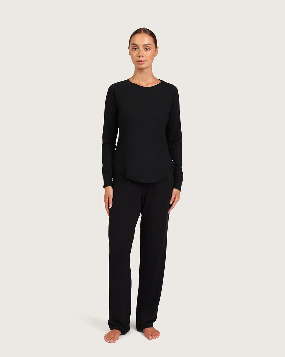 Person wearing a black long-sleeve top and pants on a beige background