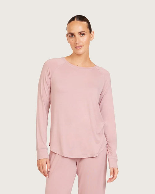 A woman modeling a dusty lilac long-sleeve top and matching pants against a light gray studio background.