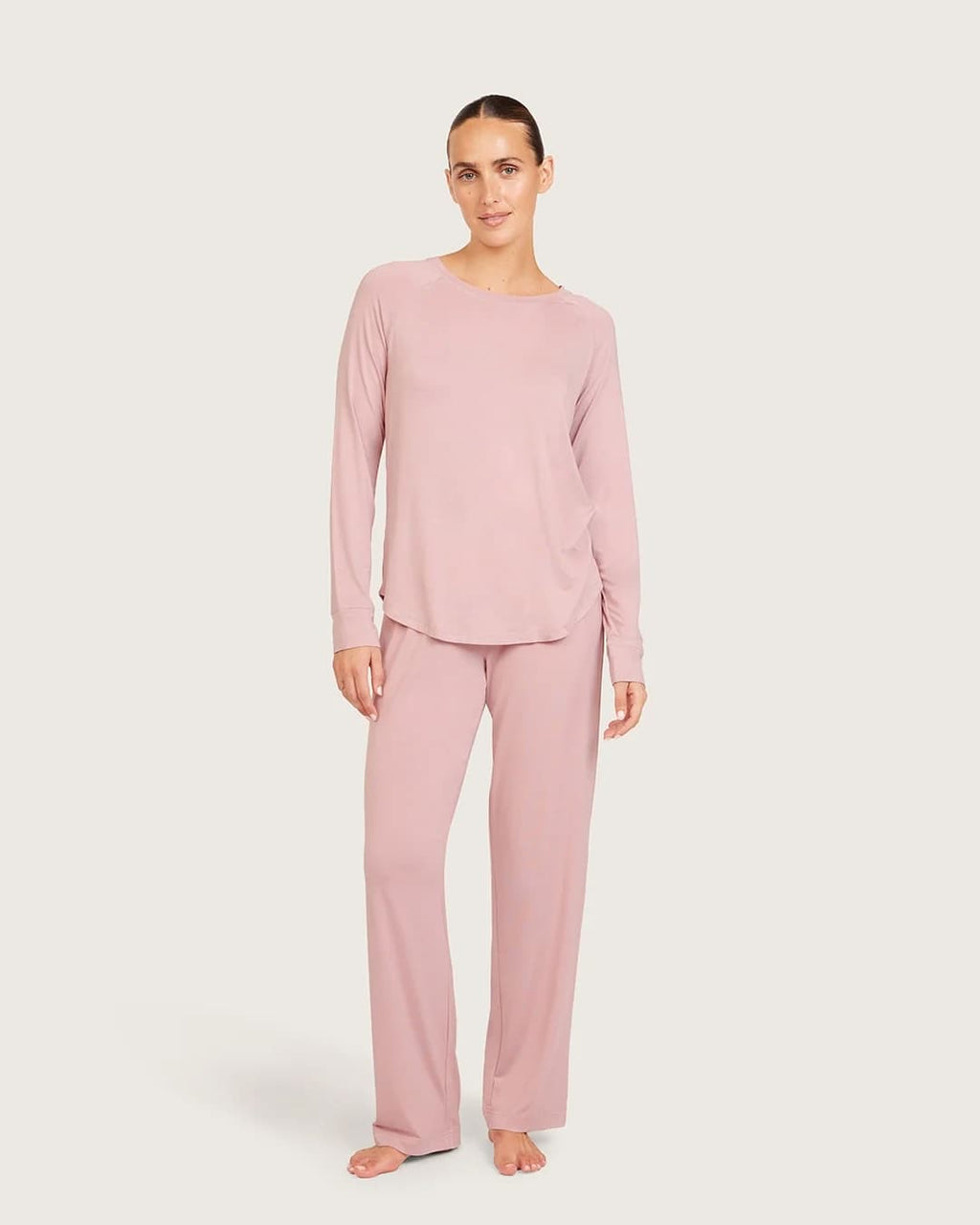 A woman modeling a two-piece dusty lilac loungewear set, consisting of a long-sleeve crewneck top and matching wide-leg pants, against a solid light gray background.