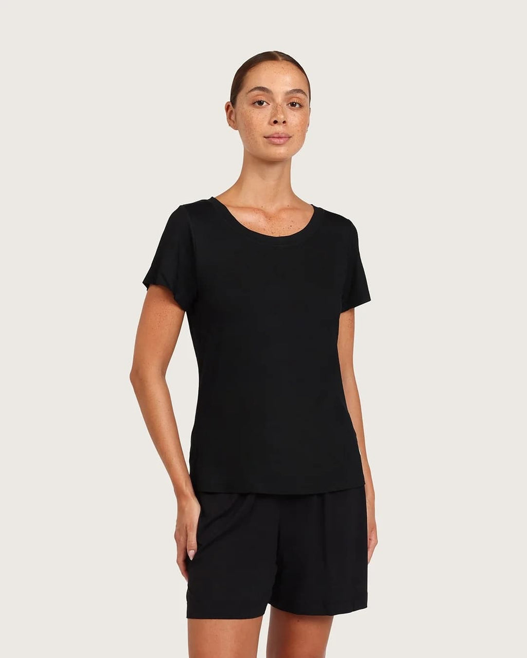 A woman modeling a black short-sleeve crewneck top with matching black shorts against a light gray studio background.